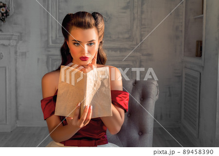 Pretty coquettish pin-up girl reads a book in retro interior 89458390