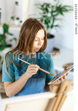 Woman artist holding paintbrush.Creative woman enjoying painting.Young beautiful woman in art studio, taking colorful paints from palette,creating masterpiece on easel, work, imagination Woman artist holding paintbrush.Creative woman enjoying painting.Young beautiful woman in art studio, taking colorful paints from palette,creating masterpiece on easel, work, imagination 89460246