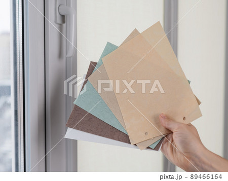 Woman holding fabric samples of roller blinds against window background. Woman holding fabric samples of roller blinds against window background. 89466164