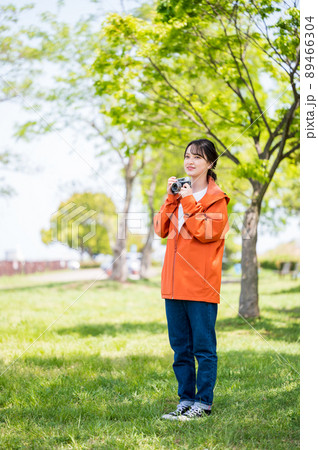 晴れた屋外でレトロなフィルムカメラで趣味の写真を撮る若い女性 89466304