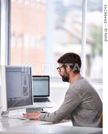 Working on the next big thing. Shot of a handsome young man working on a computer in a casual working environment. Working on the next big thing. Shot of a handsome young man working on a computer in a casual working environment. 89466744