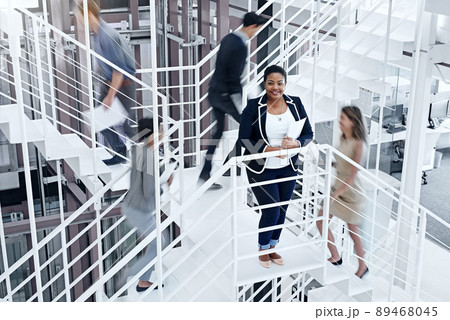 Busy making success happen. Portrait of a young professional standing on a stairs with colleagues rushing around her. Busy making success happen. Portrait of a young professional standing on a stairs with colleagues rushing around her. 89468045