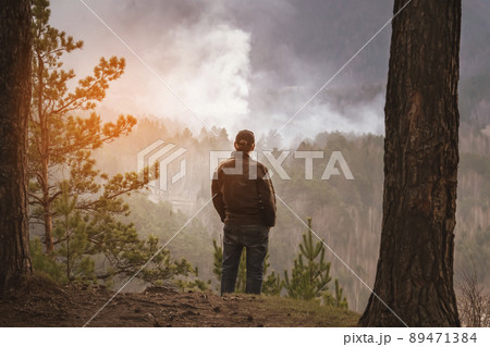 a man looks at a burning fire in the forest. tourist or forest arsonist a man looks at a burning fire in the forest. tourist or forest arsonist 89471384