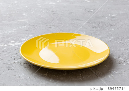 Perspective view of empty yellow plate on cement background. Empty space for your design Perspective view of empty yellow plate on cement background. Empty space for your design 89475714