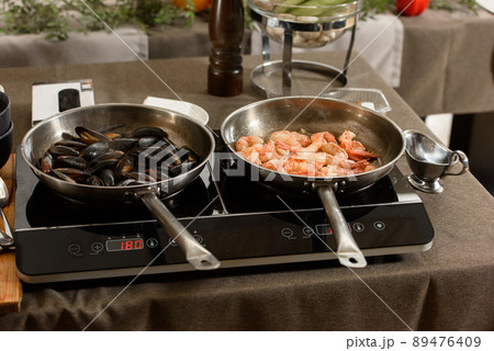 two pans with mussels and shrimp on an induction stove 89476409