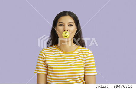 Cheerful smiling young woman with positive emoji on lips isolated on pastel purple background. Cheerful smiling young woman with positive emoji on lips isolated on pastel purple background. 89476510
