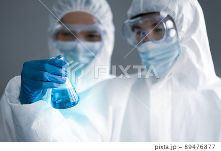 Covid-19 testing in laboratory. Two Scientists discuss about blue liquid chemical in Erlenmeyer flask. Blue lighting effect. Healthcare and medical concept. 89476877