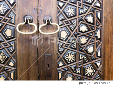 Closeup of two golden ring door knobs over an aged decorated wooden door Closeup of two golden ring door knobs over an aged decorated wooden door 89478917