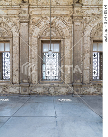 Three adjacent arched windows with decorated iron grid over white marble decorated wall Three adjacent arched windows with decorated iron grid over white marble decorated wall 89478934
