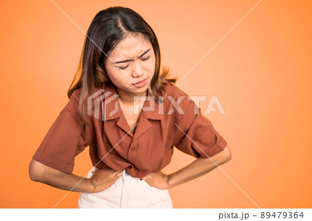 Young asian woman in pain with both hands holding stomach Young asian woman in pain with both hands holding stomach 89479364