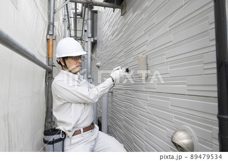 足場にのって刷毛で戸建て住宅の外壁を塗る塗装職人 89479534