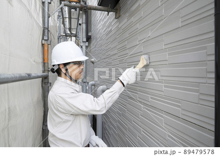 足場にのって刷毛で戸建て住宅の外壁を塗る塗装職人 89479578