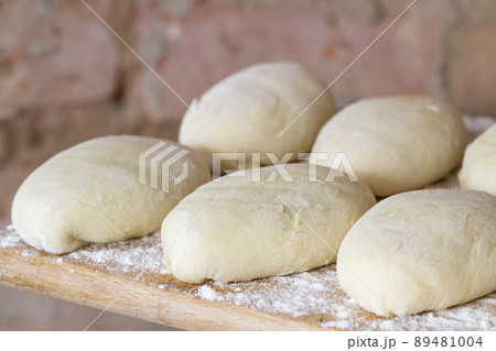 Raw homemade pies. Uncooked patties from yeast dough with stuffing are lying on a wooden plank and ready for baking. Closeup, selective focus, brick background 89481004
