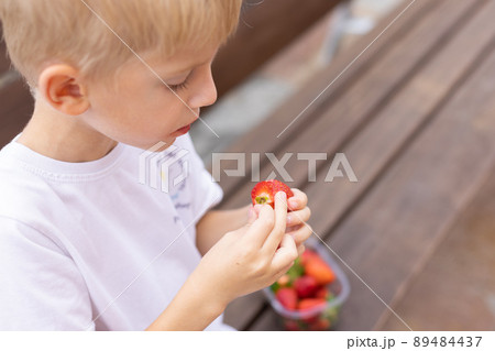 Little blonde boy eating strawberries on a bench. Little blonde boy eating strawberries on a bench. 89484437