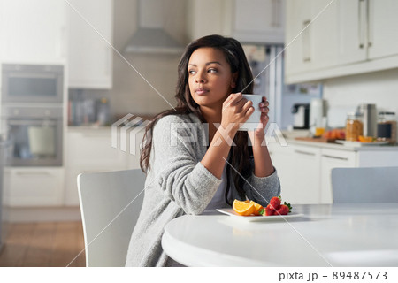 Contemplating the day that lies ahead. Shot of young woman daydreaming while enjoying breakfast in her kitchen at home. 89487573