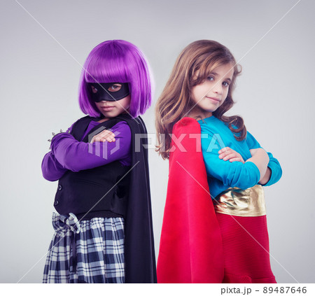 Not every girl wants to be a little princess. A studio shot of two little girls dressed up as a superhero and a villain. 89487646