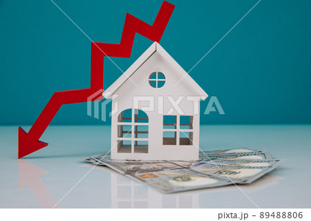Wooden house and a red arrow down with money banknotes. The concept of inflation and economic recession Wooden house and a red arrow down with money banknotes. The concept of inflation and economic recession 89488806