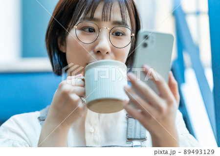 コーヒーを飲みながらスマホを使う眼鏡の女性 コーヒーを飲みながらスマホを使う眼鏡の女性 89493129