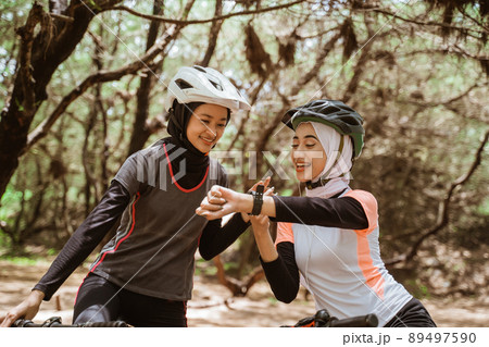 Two woman cycling and her friend looking at the watch Two woman cycling and her friend looking at the watch 89497590