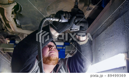 Car service. Thick ginger mechanic man standing in inspection pit and working with a tool 89499369