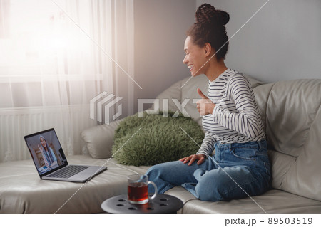 Side view of mixed-race pretty young woman smiling showing thumb up while video chatting 89503519