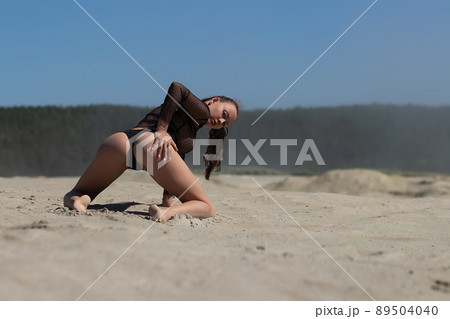 Slim woman in black underwear kneeling on sand 89504040