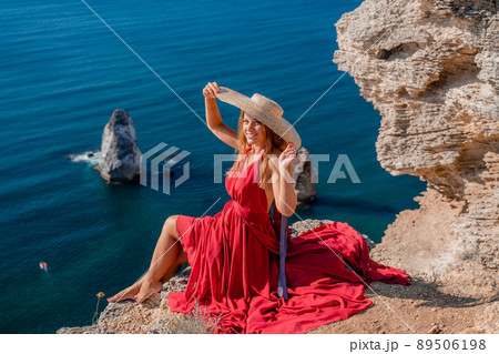 A girl with flowing hair in a long red dress sits on a rock above the sea. The stone can be seen in the sea. A girl with flowing hair in a long red dress sits on a rock above the sea. The stone can be seen in the sea. 89506198