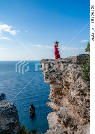 A woman in a red flying dress fluttering in the wind, against the backdrop of the sea. A woman in a red flying dress fluttering in the wind, against the backdrop of the sea. 89506206