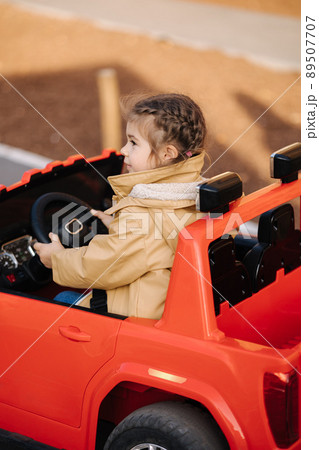 Cute little girl rides in a mini city on a red electric car jeep. Adorable little girl road in toy city. Plays for entertaiment 89507707