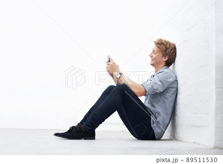 Sending an sms. A young man sitting in the studio and using his cellphone. 89511530