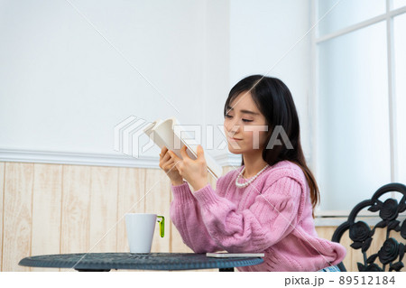 窓辺の席で本を読んでいる若い女性 窓辺の席で本を読んでいる若い女性 89512184