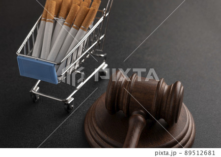 Cigarettes in shopping cart and the judges hammer on black background. Tobacco law. Illegal sale of cigarettes. Ban of cigarettes. Cigarettes in shopping cart and the judges hammer on black background. Tobacco law. Illegal sale of cigarettes. Ban of cigarettes. 89512681