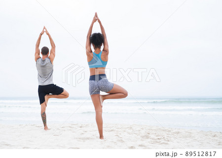 Its in staying centred that we find strength. Rearview shot of a young man and woman practising yoga together at the beach. 89512817