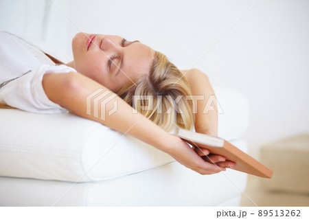 Reading makes her sleepy. An attractive young woman falling asleep on the couch with a book in hand. 89513262