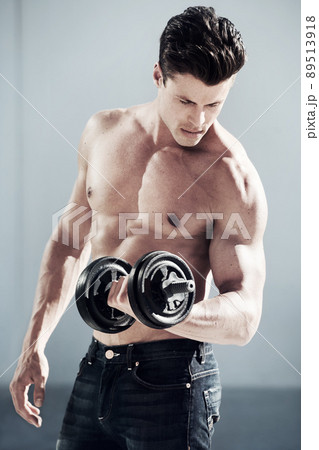 Fully focused on keeping fit. A masculine male with no shirt on lifting weights. 89513918