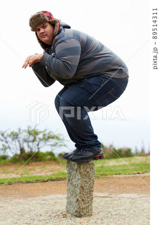 Ready to pounce. An overweight young man in winter wear balancing playfully on a post. Ready to pounce. An overweight young man in winter wear balancing playfully on a post. 89514311