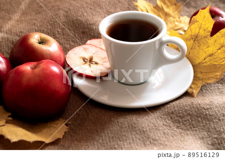 Cup of herbal tea with fresh red apples surrounded with yellow leaves on woolen textile surface 89516129