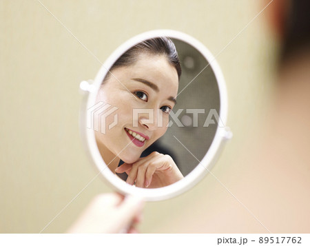 beautiful young asian woman looking at self in mirror, happy and smiling 89517762