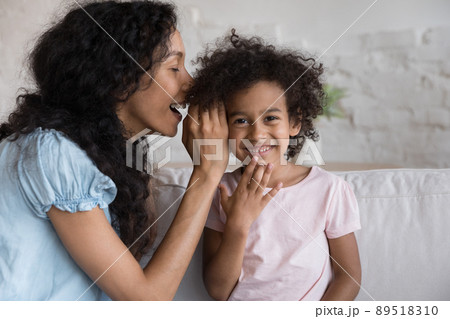 Cheerful Black mom telling secret to excited happy little girl Cheerful Black mom telling secret to excited happy little girl 89518310