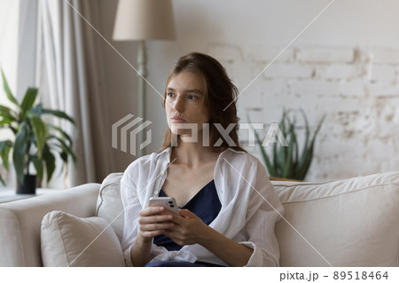 Thoughtful young freckled girl holding smartphone, looking at window away 89518464