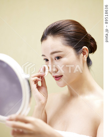 beautiful young asian woman looking in the mirror while cleansing face with a sponge beautiful young asian woman looking in the mirror while cleansing face with a sponge 89518636