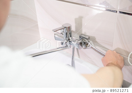 A male plumber with wrench repairs the faucet in the bathroom. 89521271