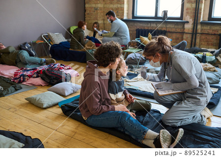 Young clinician checking up throat of little boy sitting next next to his mother 89525241