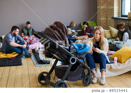 Young female sitting on couchette by stroller with her baby against refugees Young female sitting on couchette by stroller with her baby against refugees 89525441
