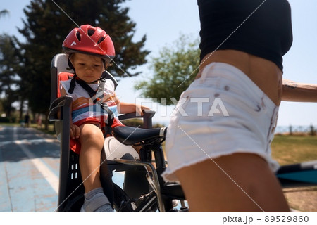 Portrait of little toddler boy with security helmet on the head sitting in bike seat and his mother Portrait of little toddler boy with security helmet on the head sitting in bike seat and his mother 89529860