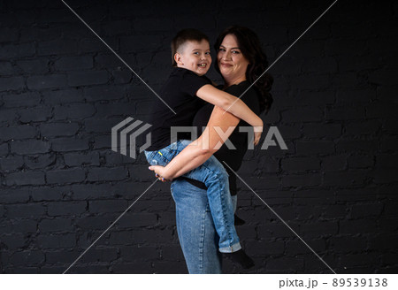 A mother in a black dress holds her son in her arms and sits on a high chair. 89539138