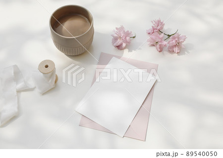 Wedding composition. Feminine spring breakfast still life. Pink Japanese cherry tree, sakura blossoms in sunlight. Blank greeting card, invitation. Cup of coffee. White dappled table background. 89540050