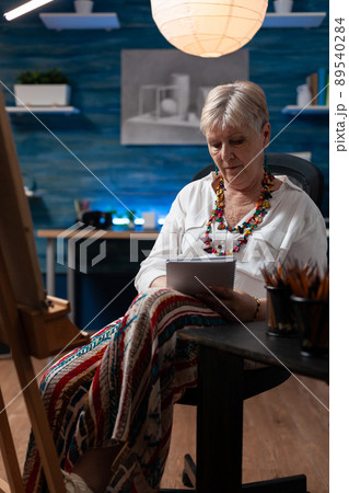 Elderly artist doing sketch on notebook for practice before drawing on easel in home art studio. Senior hobby art creator taking notes keeping journal of learning progress in workshop. Elderly artist doing sketch on notebook for practice before drawing on easel in home art studio. Senior hobby art creator taking notes keeping journal of learning progress in workshop. 89540284