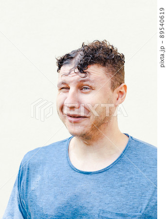 Astonished shocked wet young caucasian man with curly hair in blue t-shirt looking away and crying on white background. Portrait, rain, vertical photo. 89540619