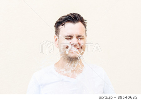 Wet young caucasian man in white t-shirt with closed eyes in water splash. Portrait, stress shock concept, lifestyle 89540635